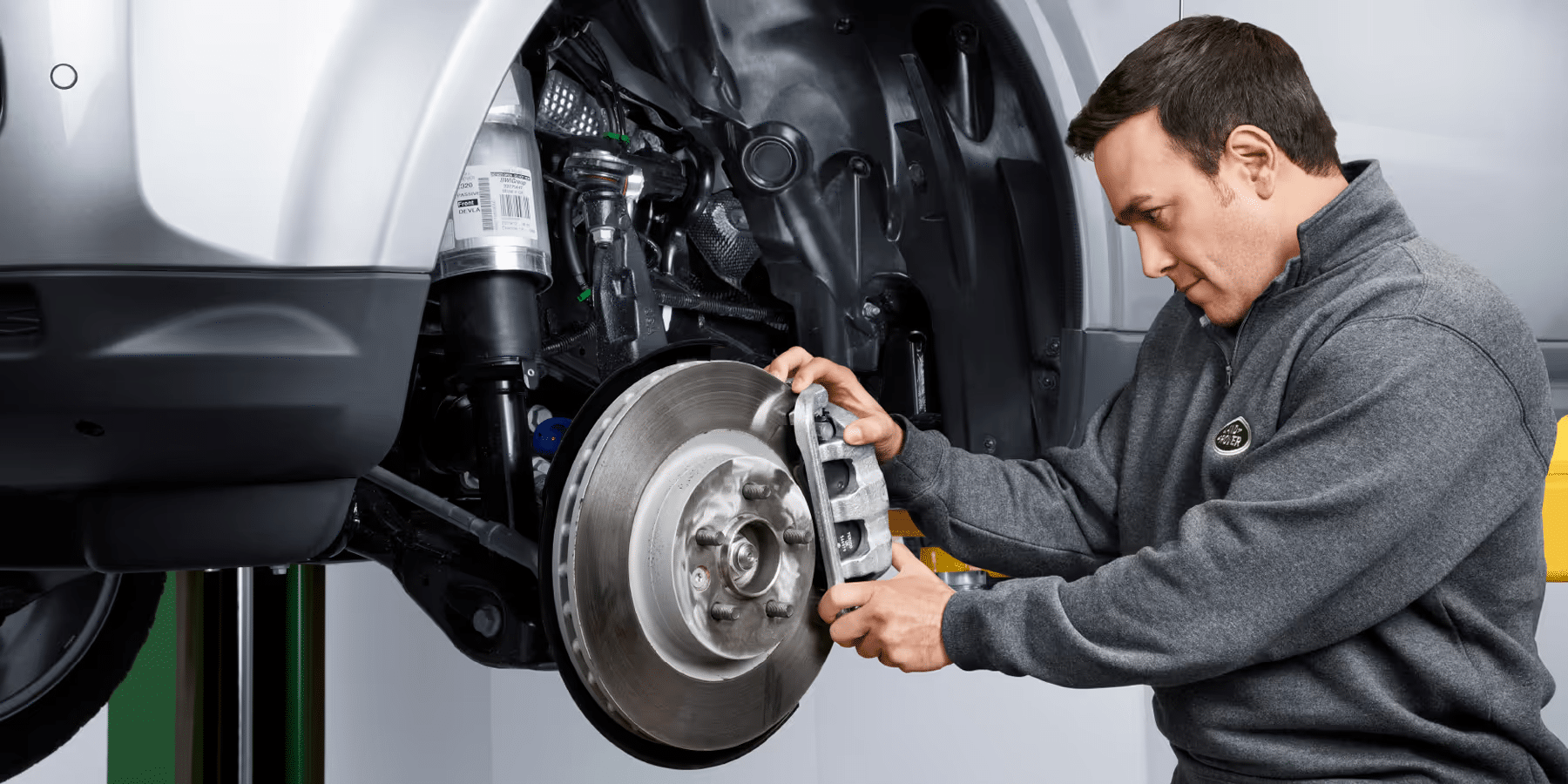 Mechanic inspecting a car's brake system, focusing on the brake caliper and rotor.