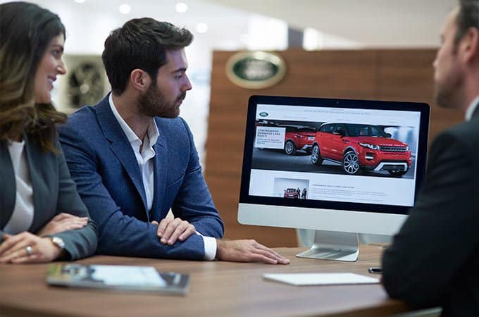 People discussing a red Land Rover displayed on a computer screen in an office setting.