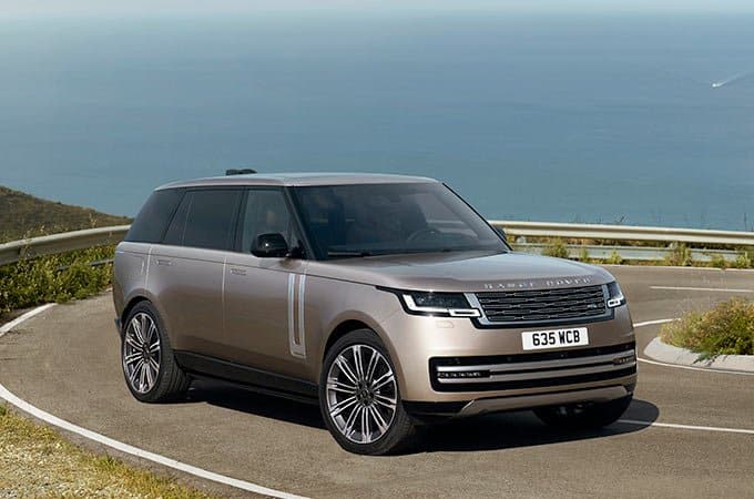A sleek, modern SUV with a beige finish parked on a coastal road with an ocean backdrop.