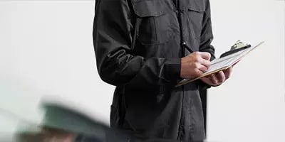 Person in black jacket writing on a clipboard, performing an inspection or survey.