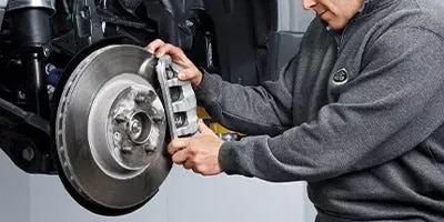 Mechanic inspecting a car's brake system, focusing on the brake disc and caliper.