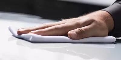 Hand wiping car surface with a white cloth for cleaning and polishing.