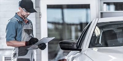 Mechanic inspecting a car, taking notes on a clipboard at an auto repair shop.