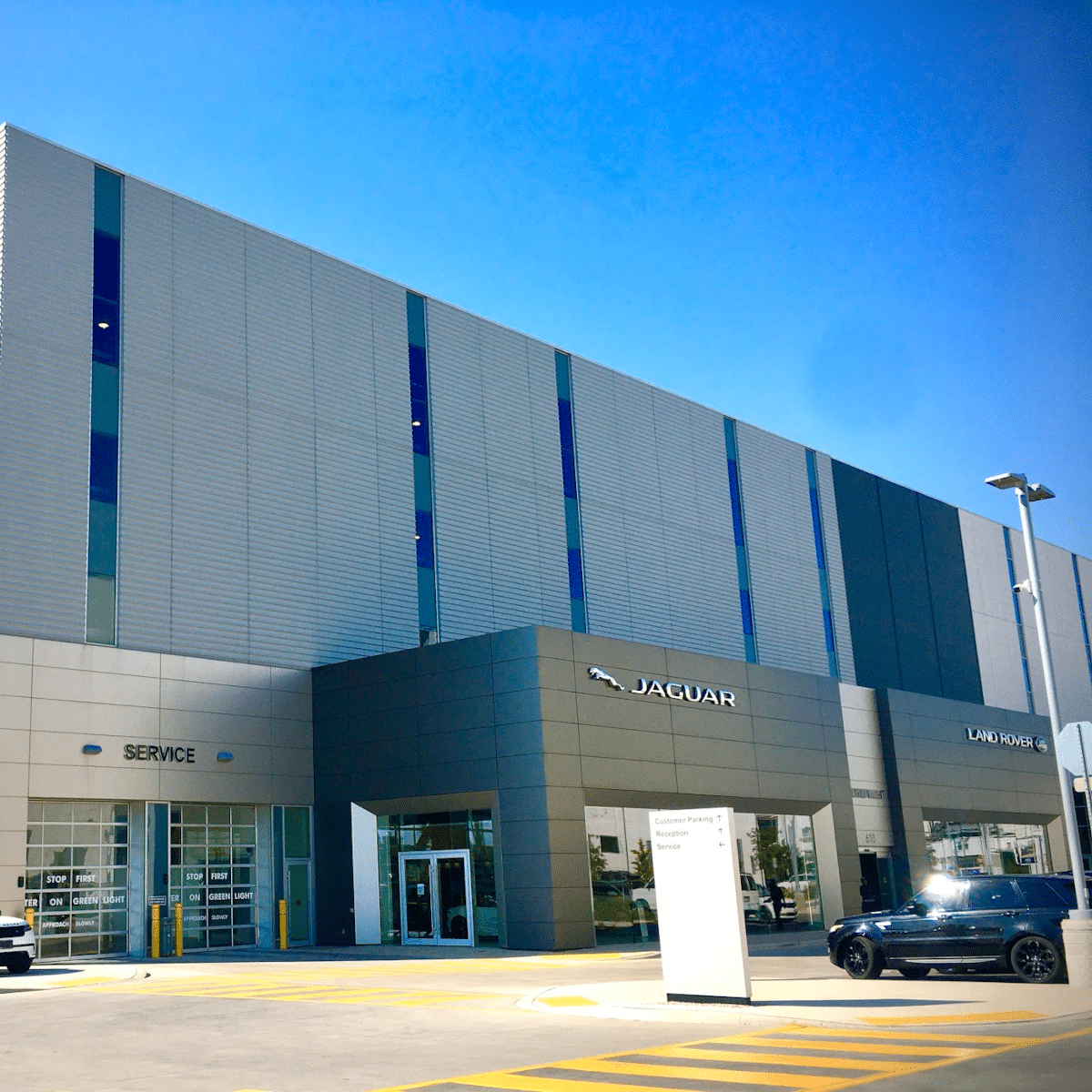 Exterior of a Jaguar Land Rover dealership with service entrance and cars parked outside.